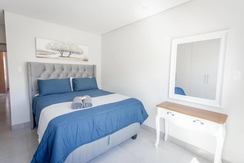 Bright bedroom with blue bedding, gray upholstered headboard, and modern white vanity