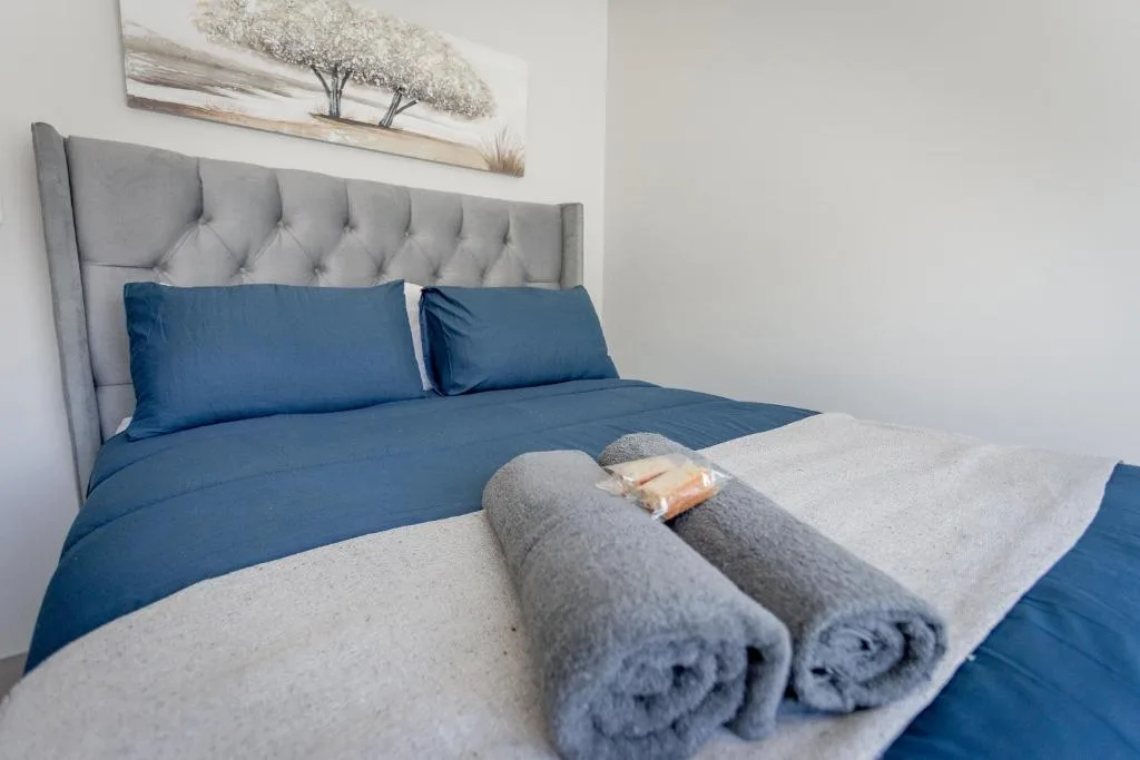 Neatly made bed with blue linens and gray upholstered headboard, towels laid out