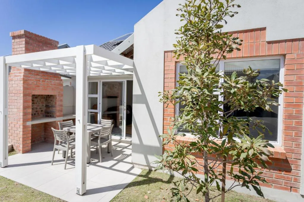 Modern white pergola patio with seating, brick fireplace, and landscaping