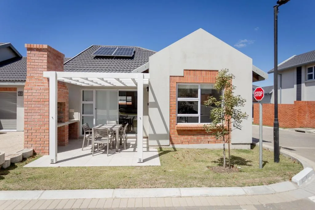 Modern white and brick cottage with covered patio and young tree in front yard