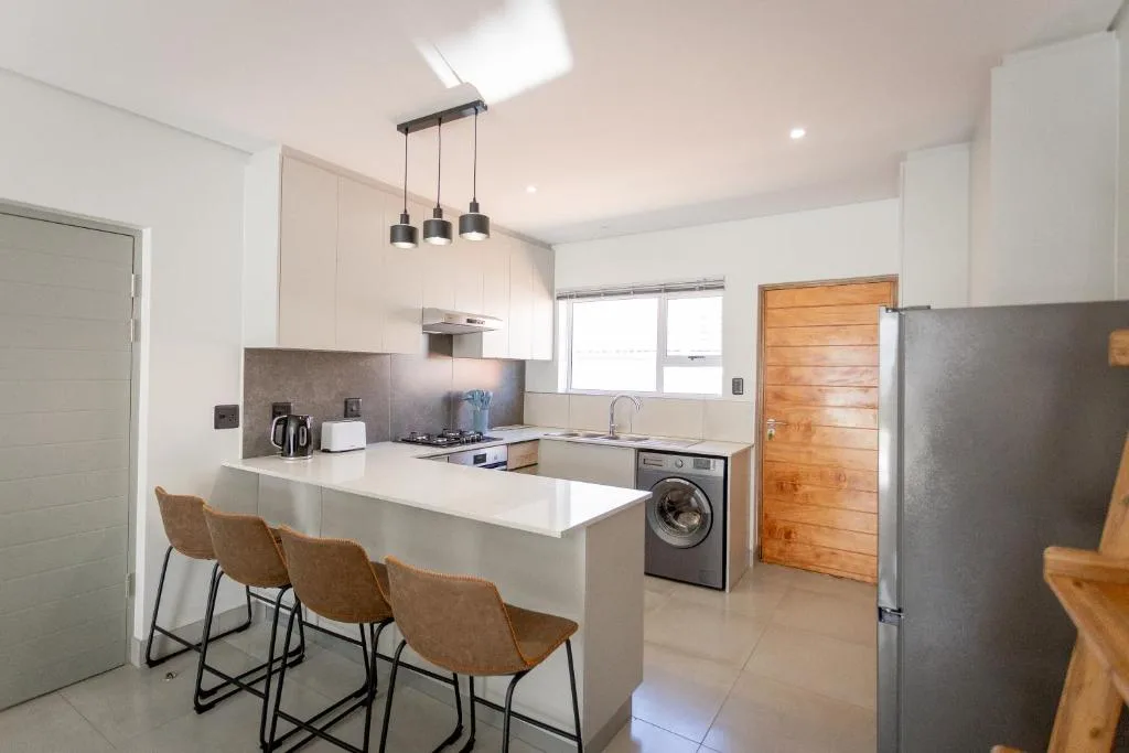 Modern kitchen with white cabinetry, gas stove, washing machine, and breakfast counter seating