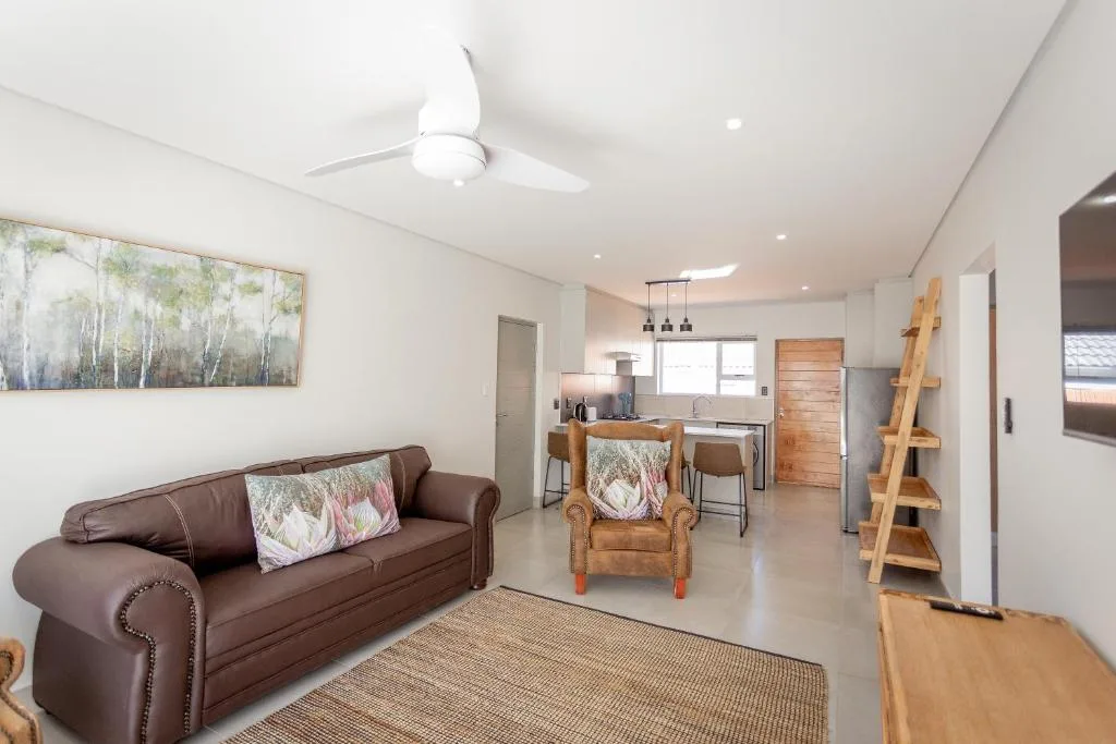Modern lounge with brown sofa, wooden chair, and open-plan kitchen beyond
