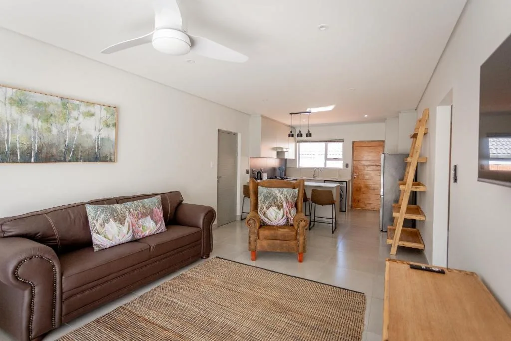 Open-plan lounge with brown sofa, wooden armchair, and kitchen visible beyond