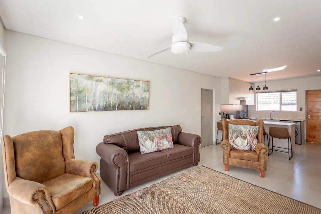 Open-plan lounge with brown leather sofa and tan armchairs, kitchen visible beyond