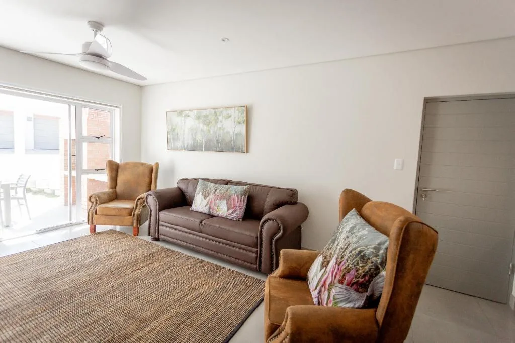 Spacious lounge with brown leather sofa, wingback chairs, and artwork