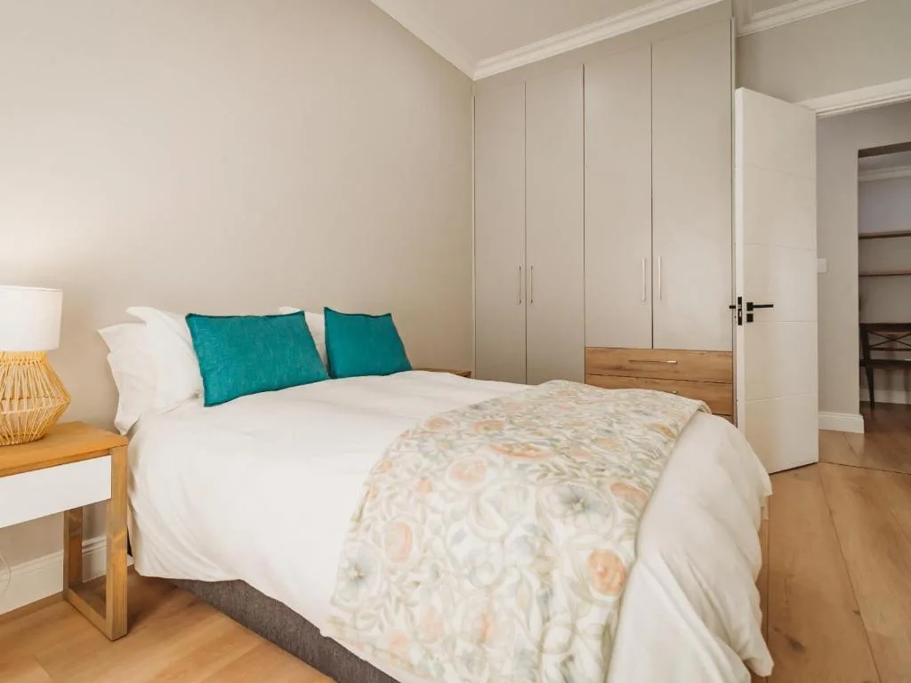 Bright bedroom with queen bed, turquoise pillows, wooden nightstand, and built-in wardrobes