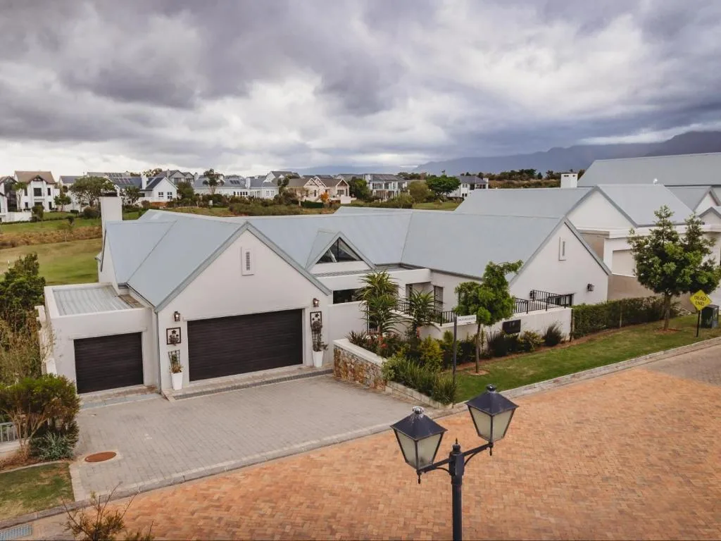 Modern white Cape-style home with double garage and manicured gardens, suburban setting