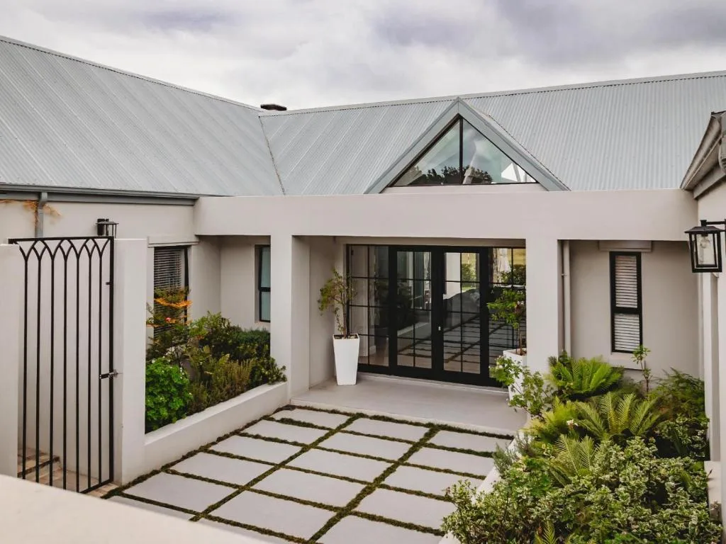 Modern white cottage exterior with metal roof and manicured garden entrance