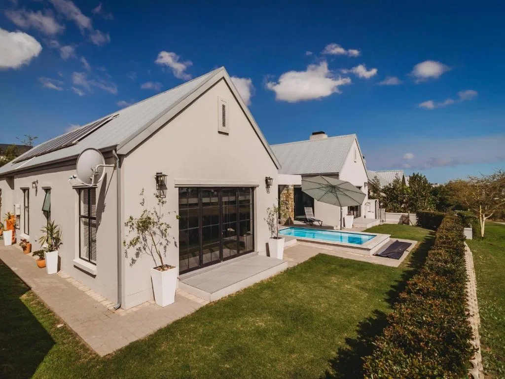 Modern white farmhouse with pool, manicured gardens, and blue sky