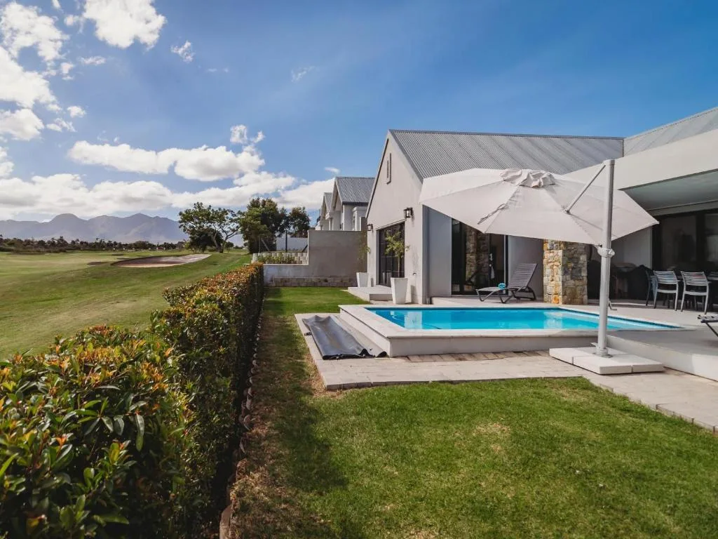 Modern swimming pool with white umbrella on paved deck beside manicured gardens