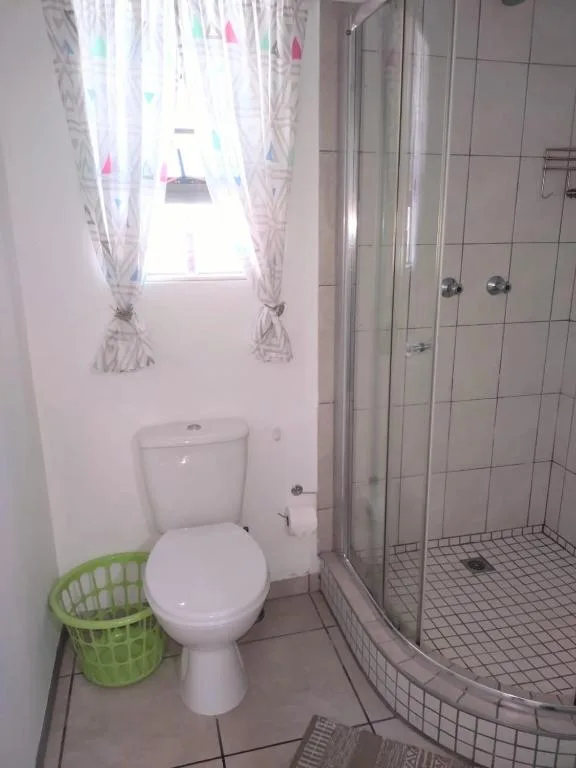 Clean bathroom with toilet, shower enclosure, and window with colorful curtains