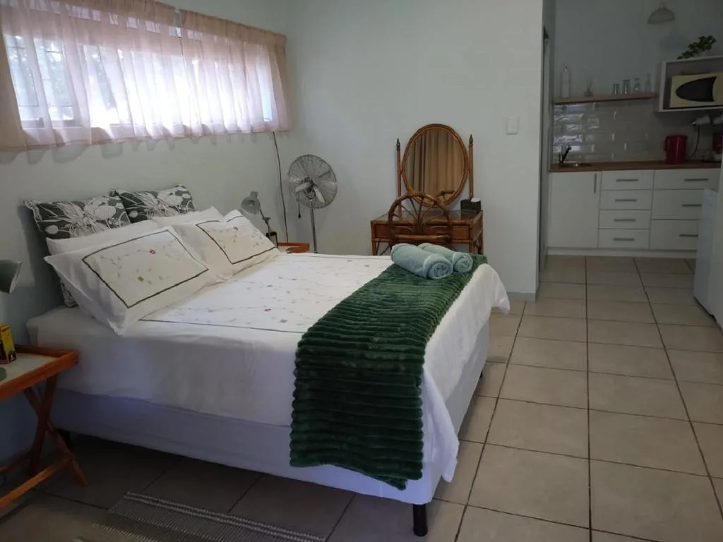 Bright bedroom with white bed, green throw blanket, and kitchenette visible