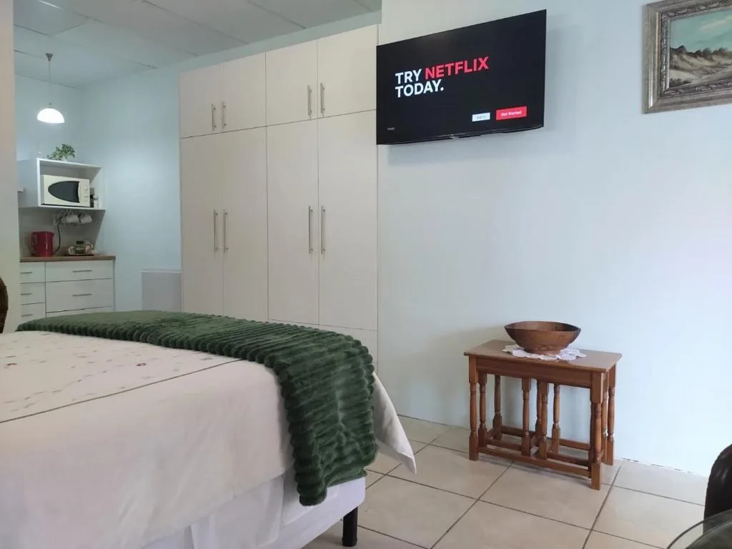 Modern bedroom with white storage, mounted TV, and green bedding throw