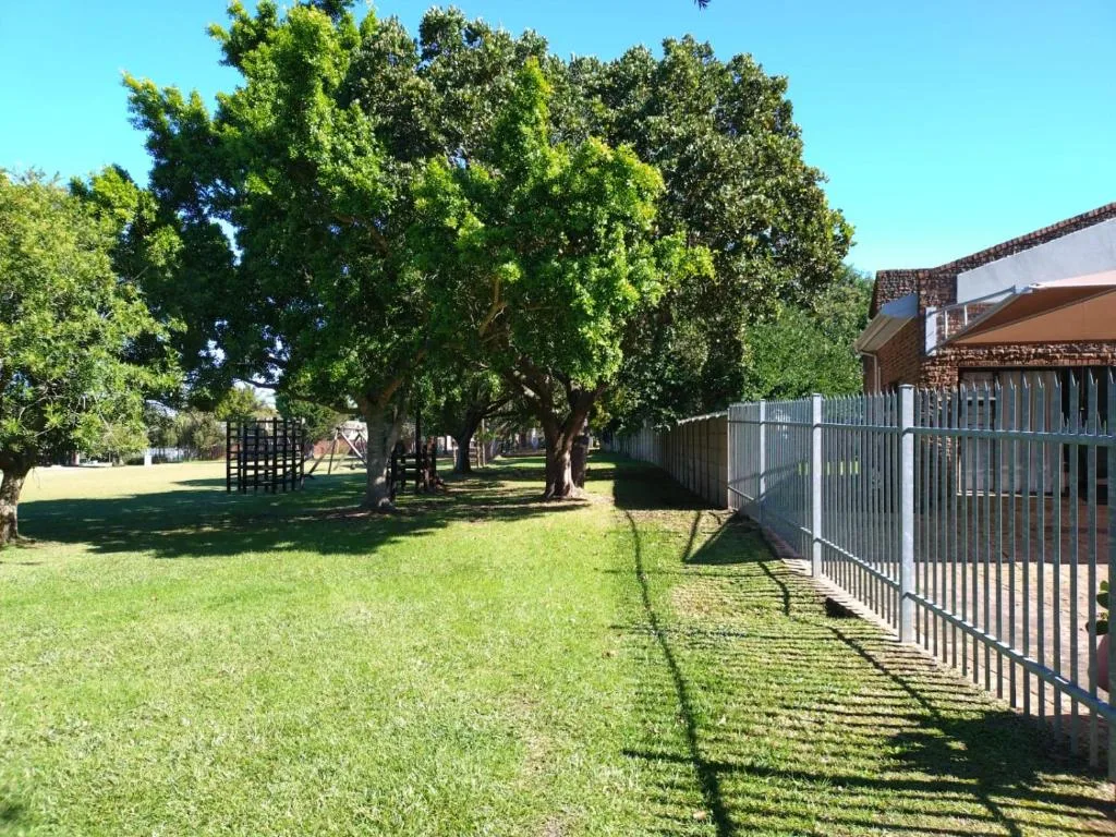 Spacious garden with mature trees, fencing, and stone building