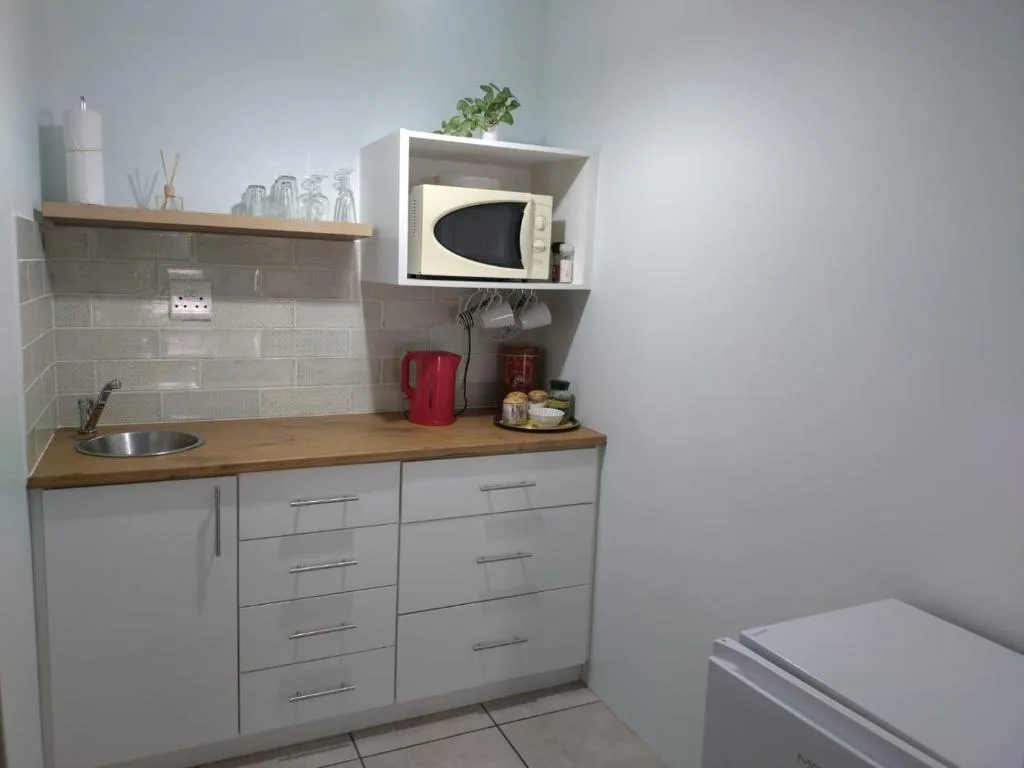 Compact kitchenette with white cabinetry, wooden countertop, and microwave