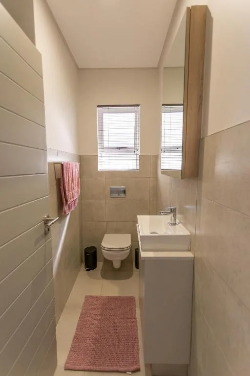 Modern bathroom with white tiles, toilet, vanity sink, and windows