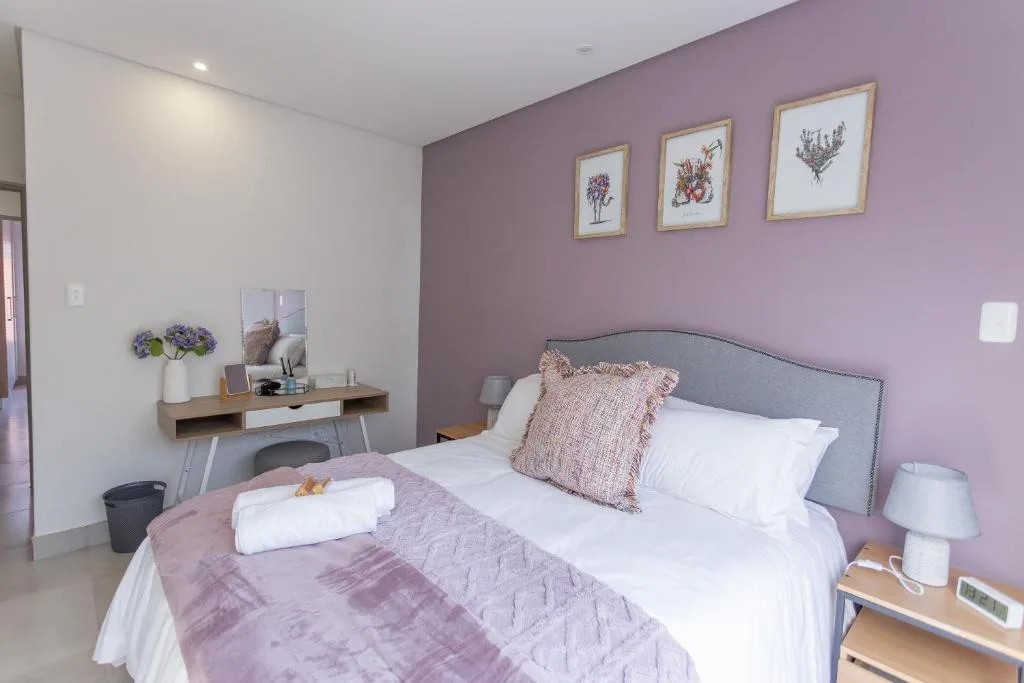 Bright bedroom with purple accent wall, queen bed, and botanical artwork