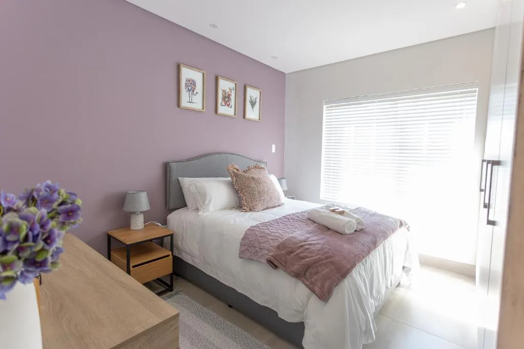 Modern bedroom with purple accent wall, queen bed, and bright natural light