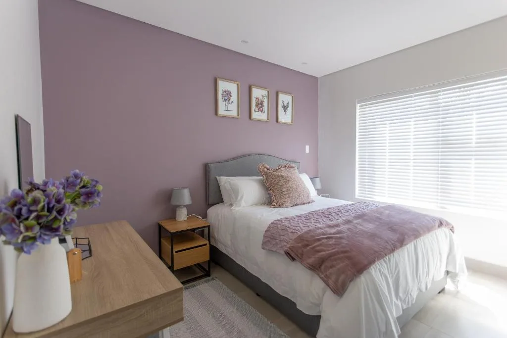 Bedroom with mauve accent wall, queen bed, and modern furnishings