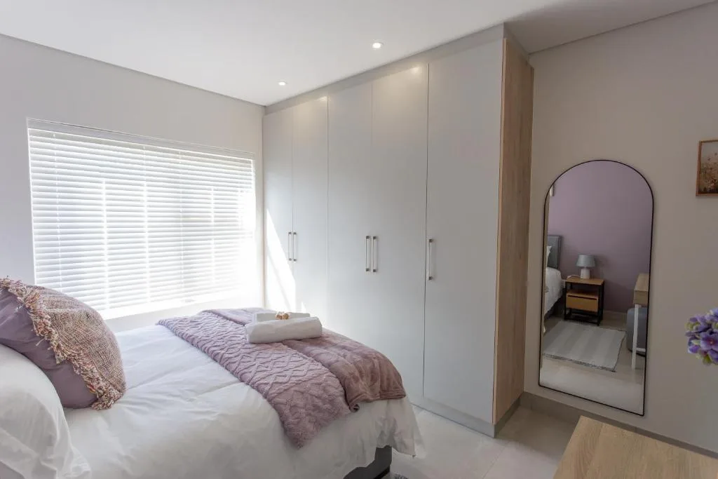 Modern bedroom with bed, white built-in wardrobes, and arched mirror