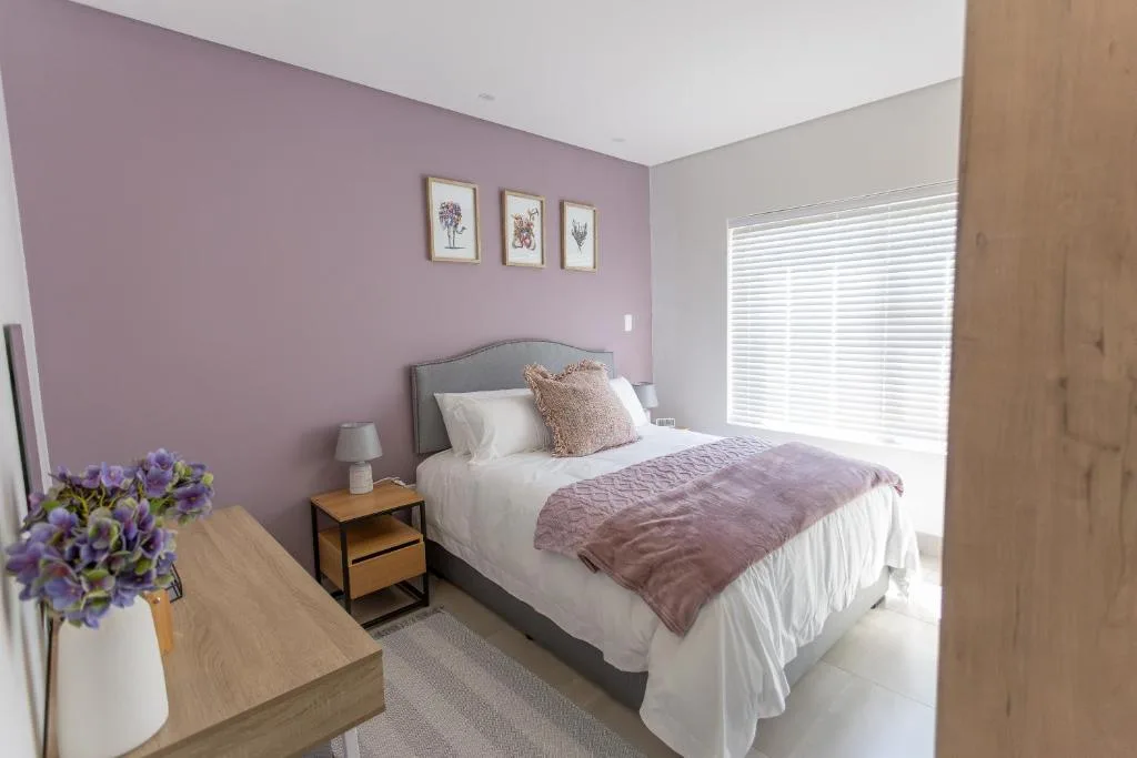 Modern bedroom with purple accent wall, queen bed, and fresh floral arrangement