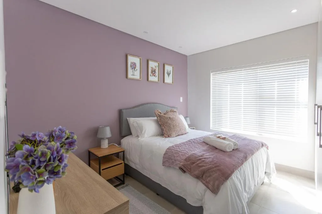 Bright bedroom with purple accent wall, queen bed, and large windows