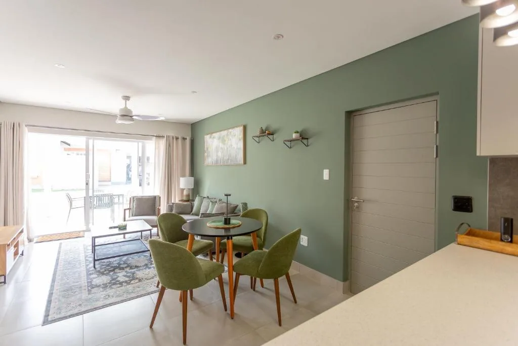 Modern dining area with green chairs and round wooden table, sage green walls