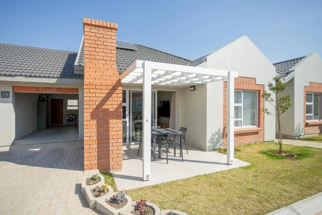 Modern townhouse exterior with white pergola, brick chimney, and manicured garden