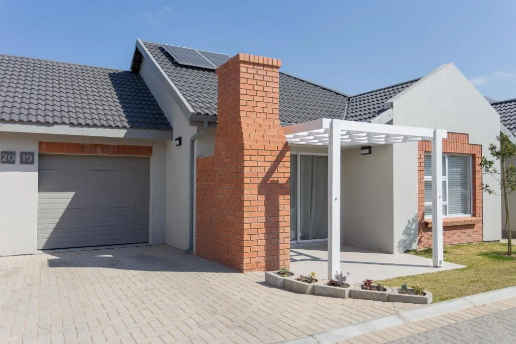 Modern townhouse with white walls, brick chimney, garage, and pergola entrance