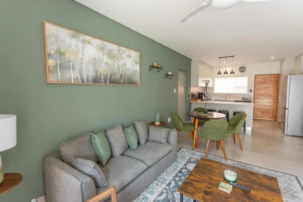 Open-plan lounge with gray sofa, green accent wall, and dining area beyond