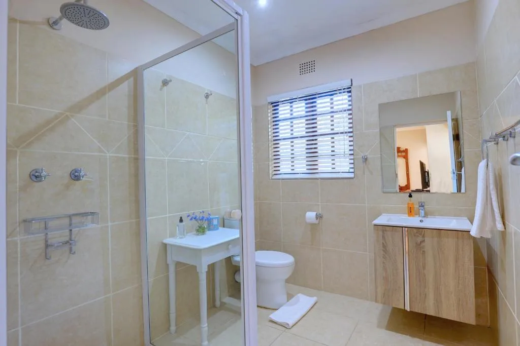 Modern bathroom with rainfall shower, vanity sink, toilet, and large mirror