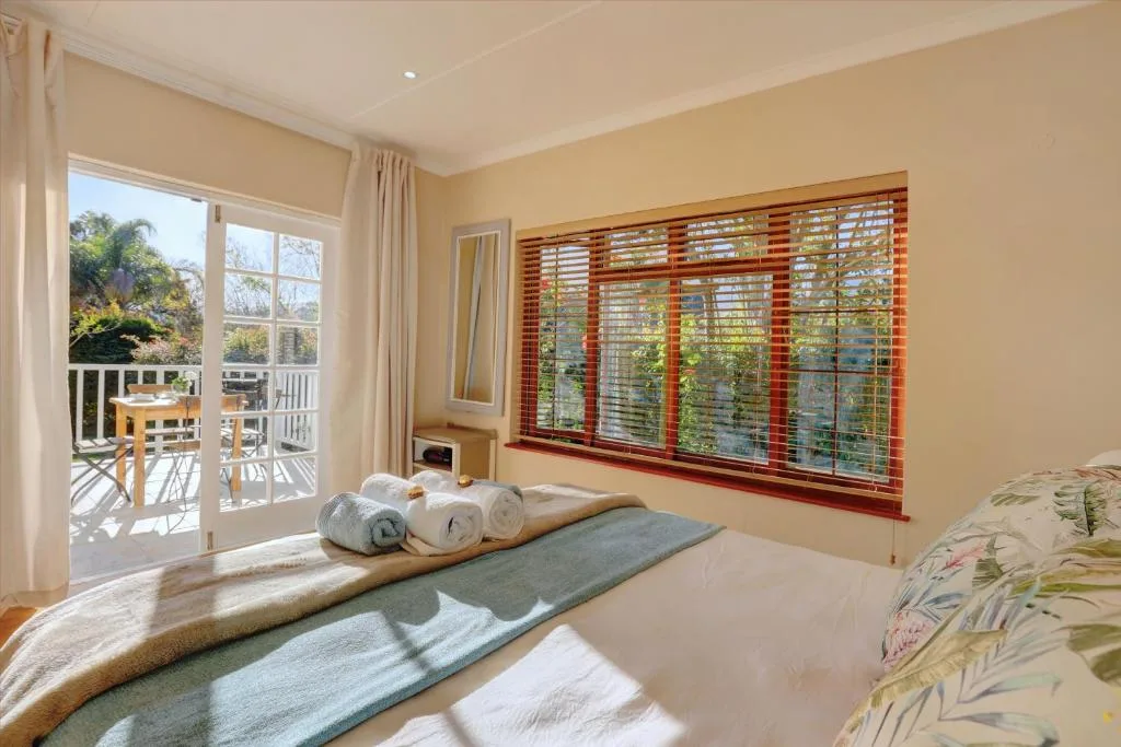 Bright bedroom with bed, rolled towels, and garden views through large windows