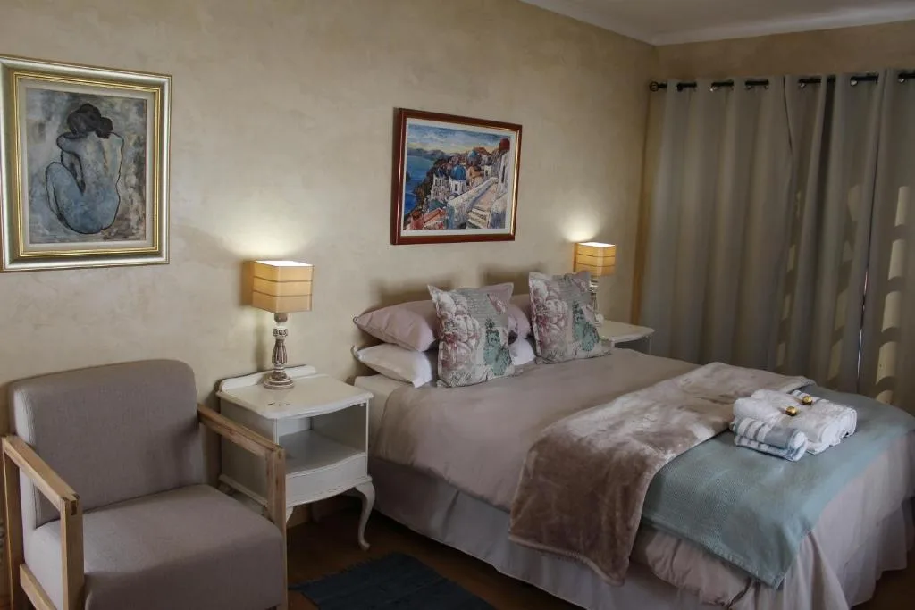Spacious bedroom with queen bed, framed artwork, bedside lamps, comfortable seating chair