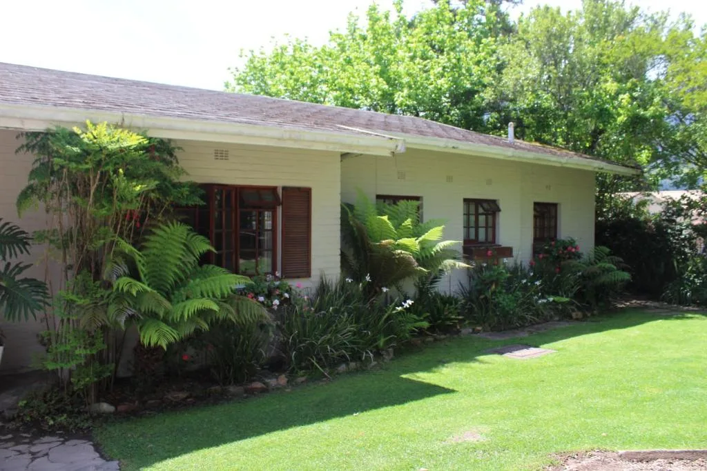 Cream-coloured cottage with dark wooden windows and lush tropical garden landscaping