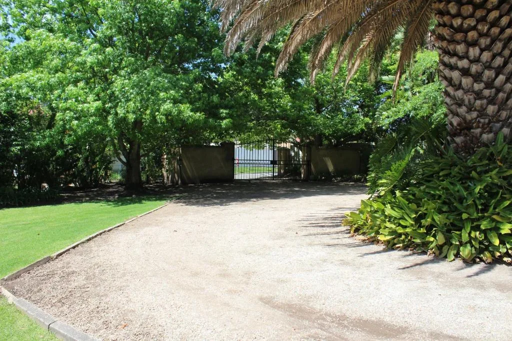 Property driveway with mature trees, manicured lawn, and gated entrance