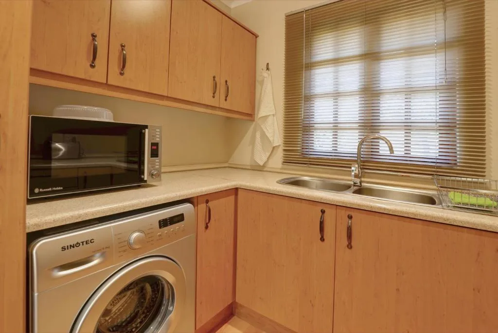 Compact kitchen with wooden cabinetry, washing machine, microwave, and sink
