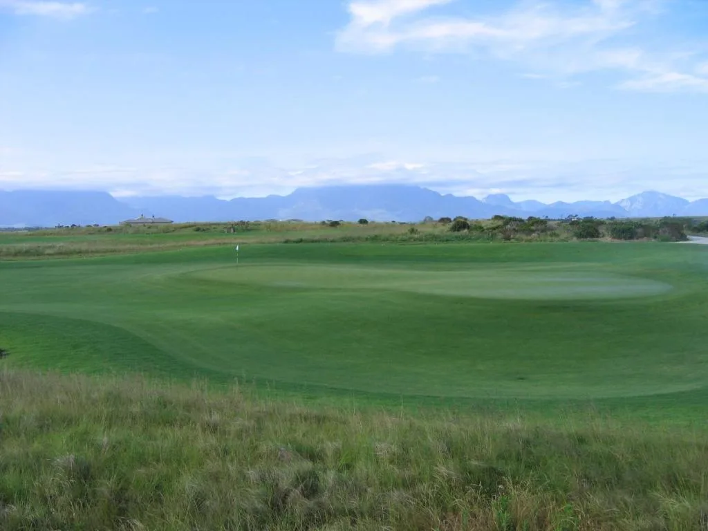 Golf course landscape with mountain range backdrop under blue sky