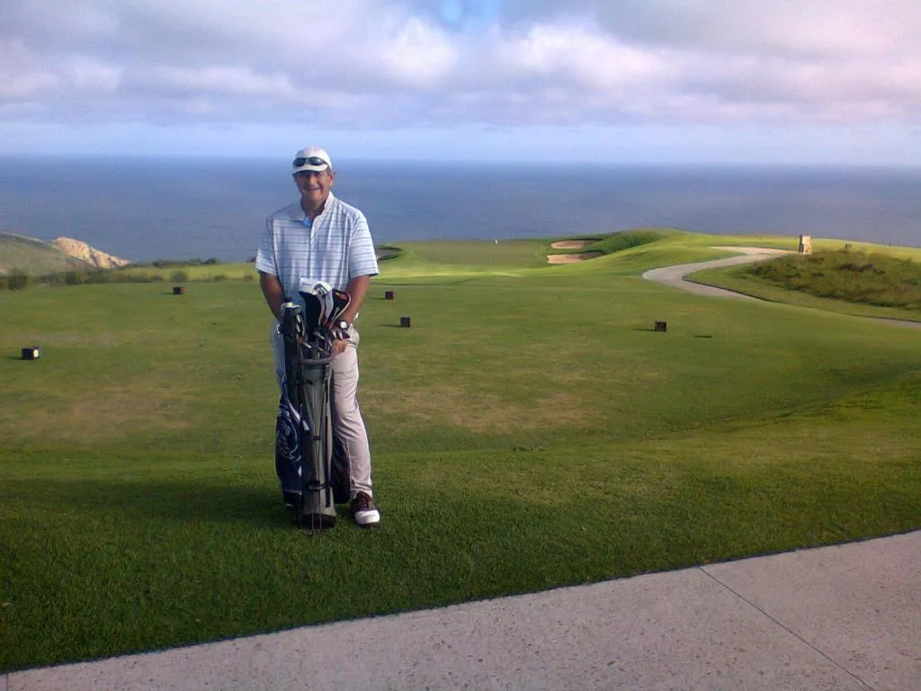 Golfer with clubs overlooking pristine coastal landscape and ocean horizon