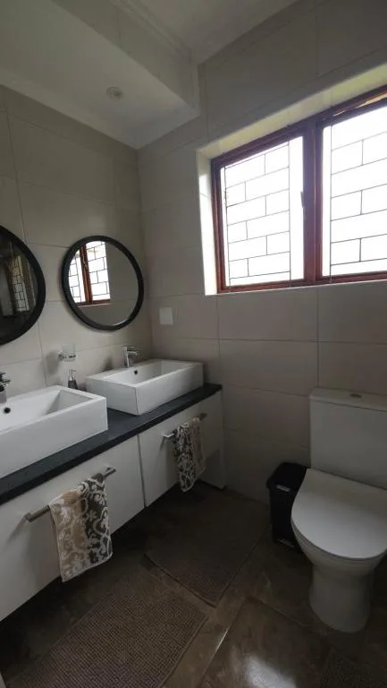 Modern bathroom with double vanity sinks, round mirrors, and toilet