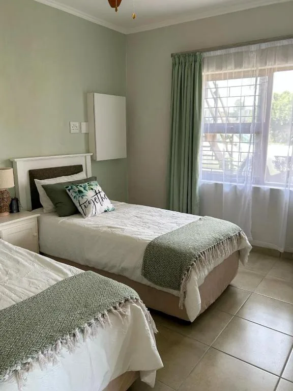 Twin bedroom with green accents, natural light, and garden views through windows