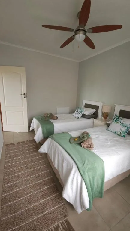 Twin bedroom with white beds, green throws, ceiling fan, and door
