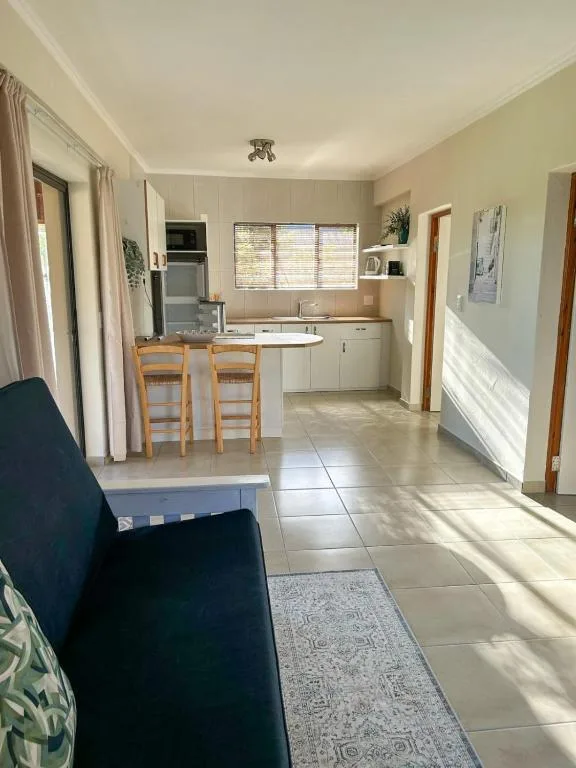 Open-plan lounge and kitchen area with sofa, dining chairs, and natural light