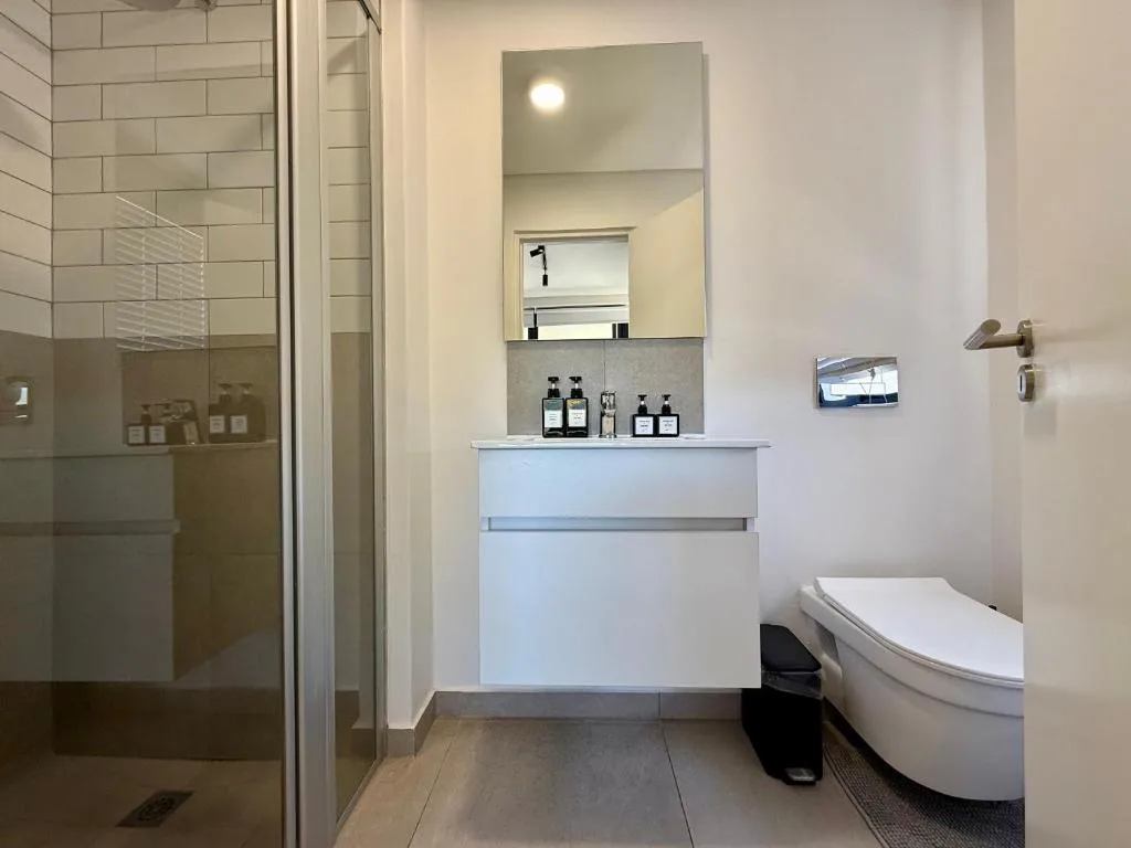 Modern bathroom with white vanity, mirror, toilet, and walk-in shower enclosure