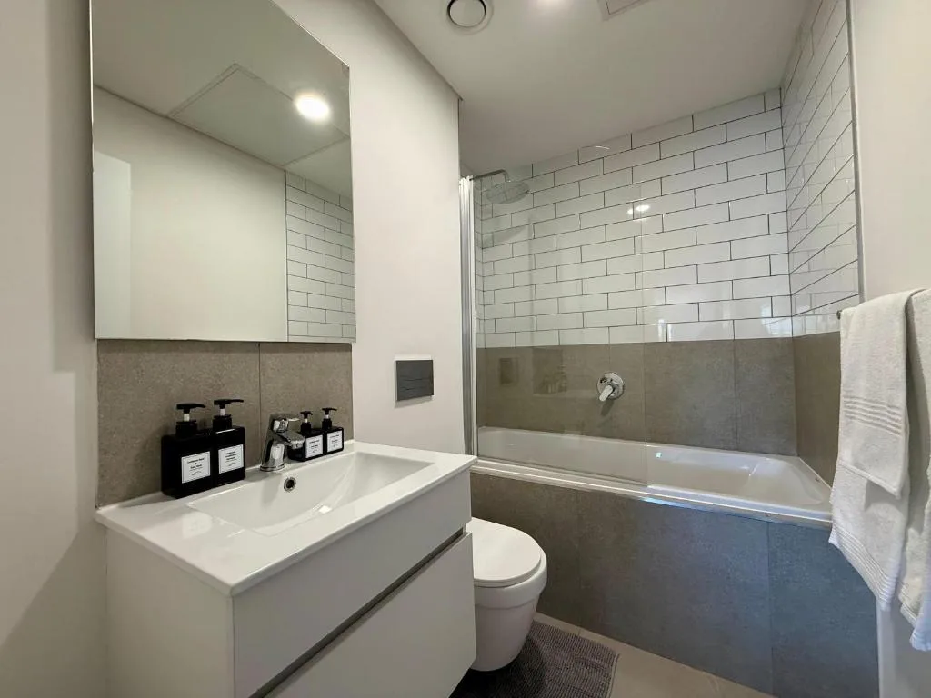 Modern bathroom with white vanity, mirror, toilet, and bathtub with subway tiles