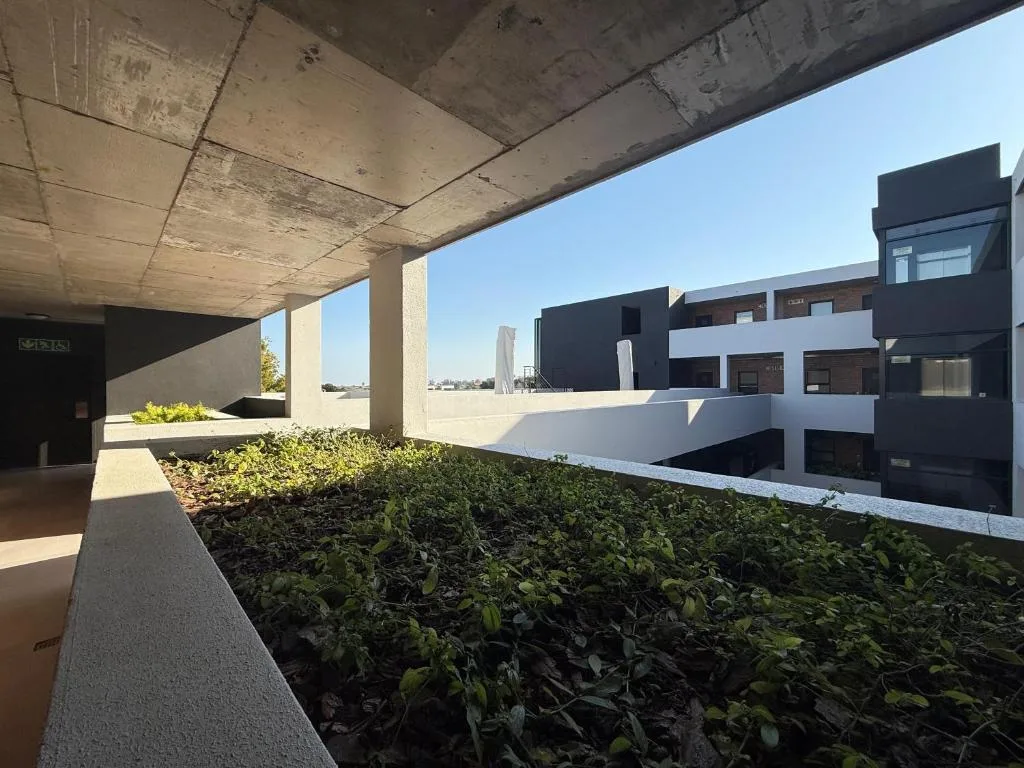 Modern apartment courtyard with concrete beams, landscaped garden beds, white railings