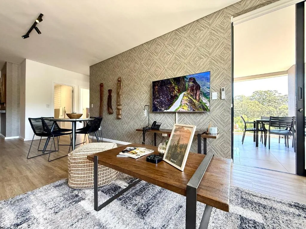 Modern lounge with wooden table, patterned wallpaper, TV, and deck access