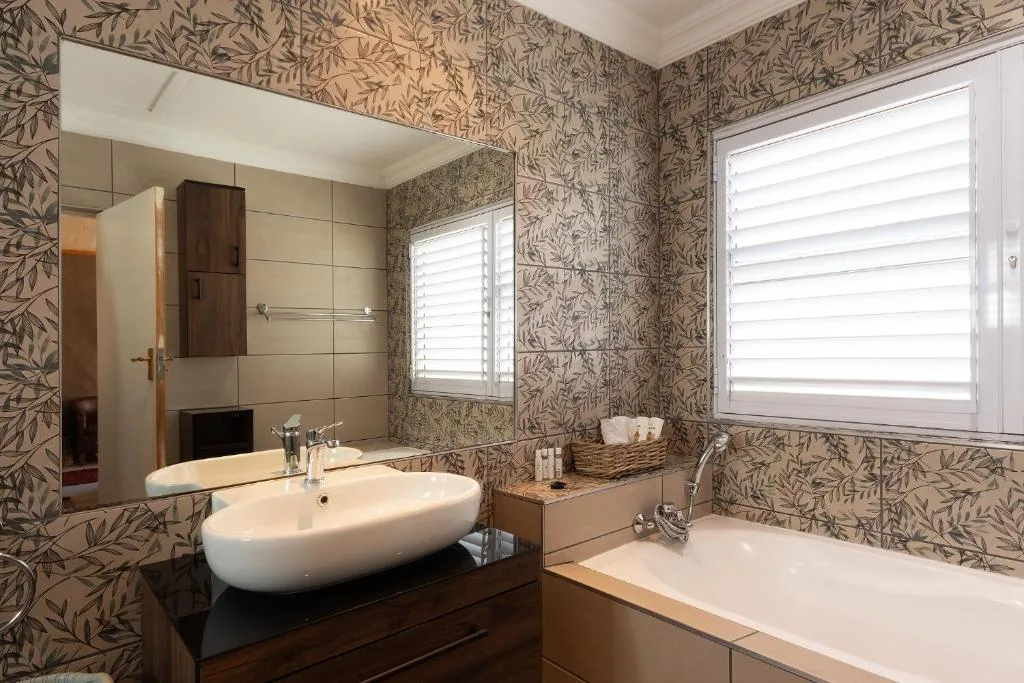 Modern bathroom with oval sink, bathtub, and leafy wallpaper design
