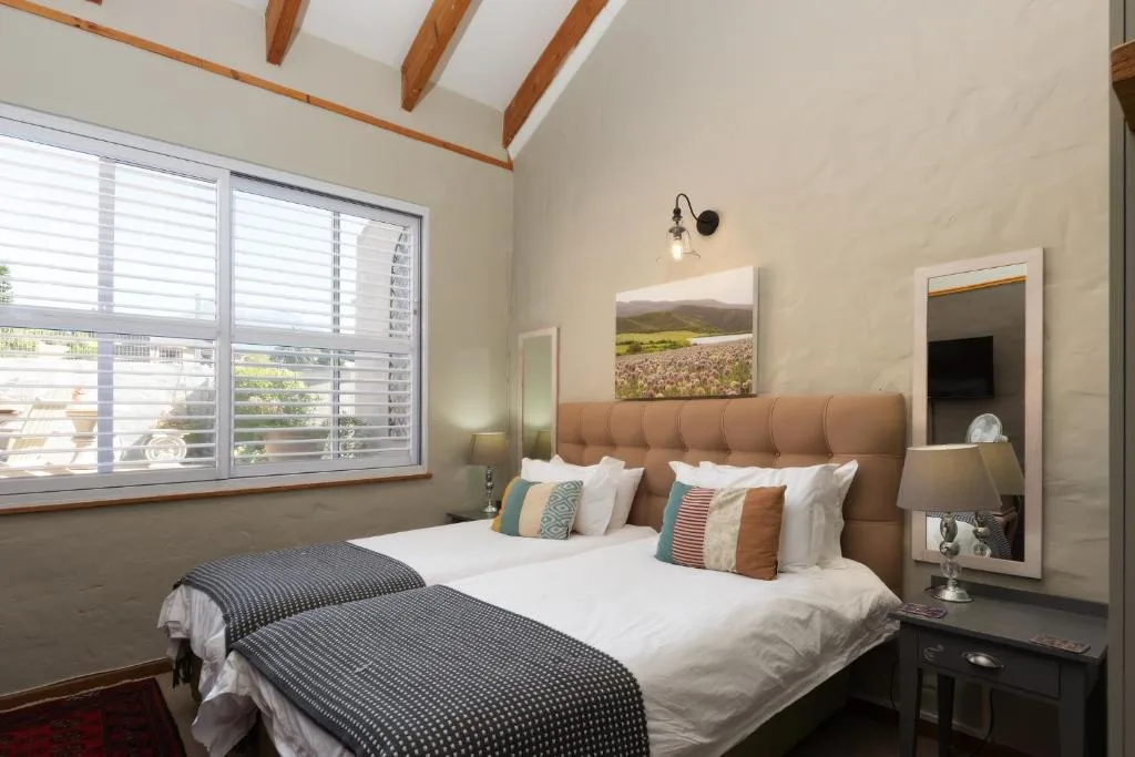 Bright bedroom with twin beds, exposed wooden beams, and garden view windows
