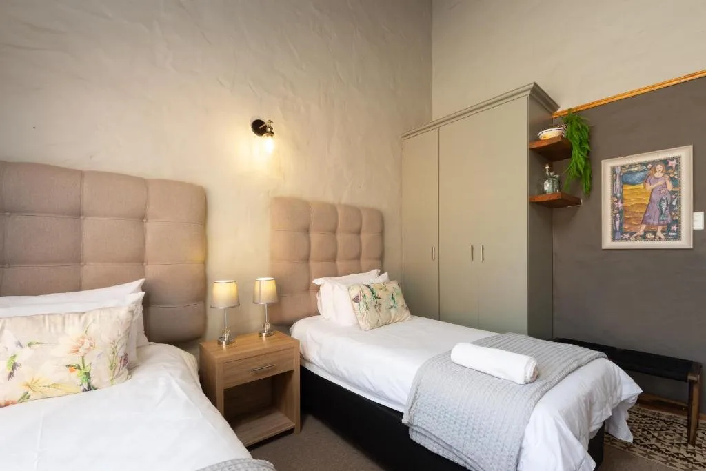 Bright bedroom with two single beds and padded headboards, nightstand lighting, and storage.