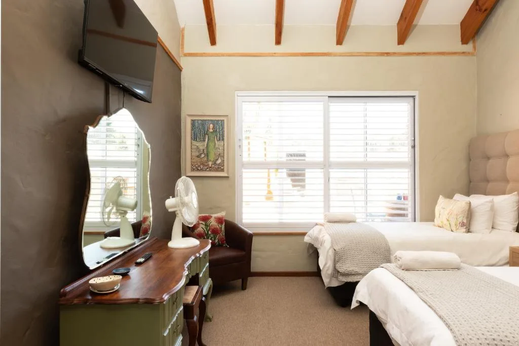 Bright bedroom with two beds, desk, TV, and large windows overlooking garden